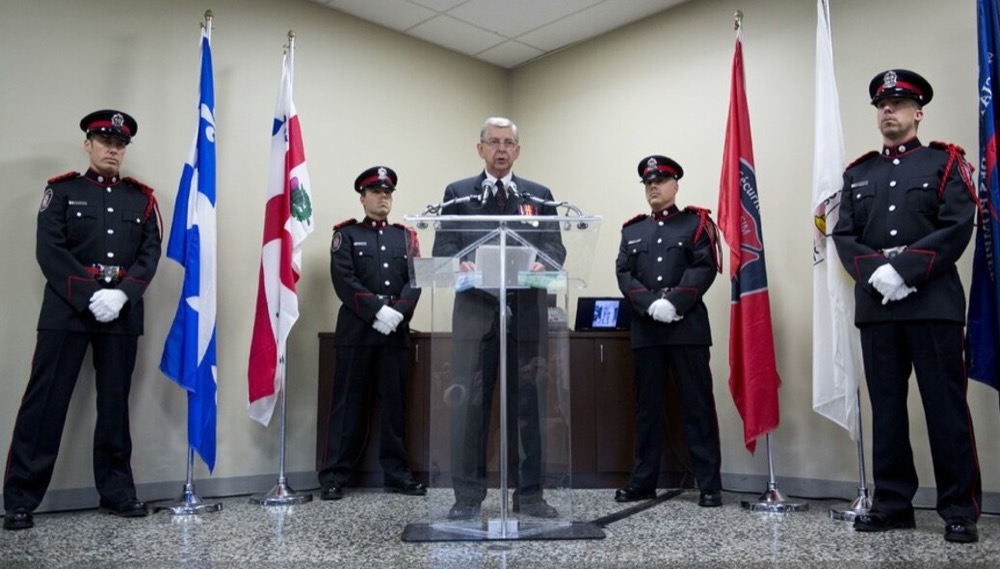 Gérald Laplante au lutrin, entouré d'une garde d'honneur de pompiers en uniforme